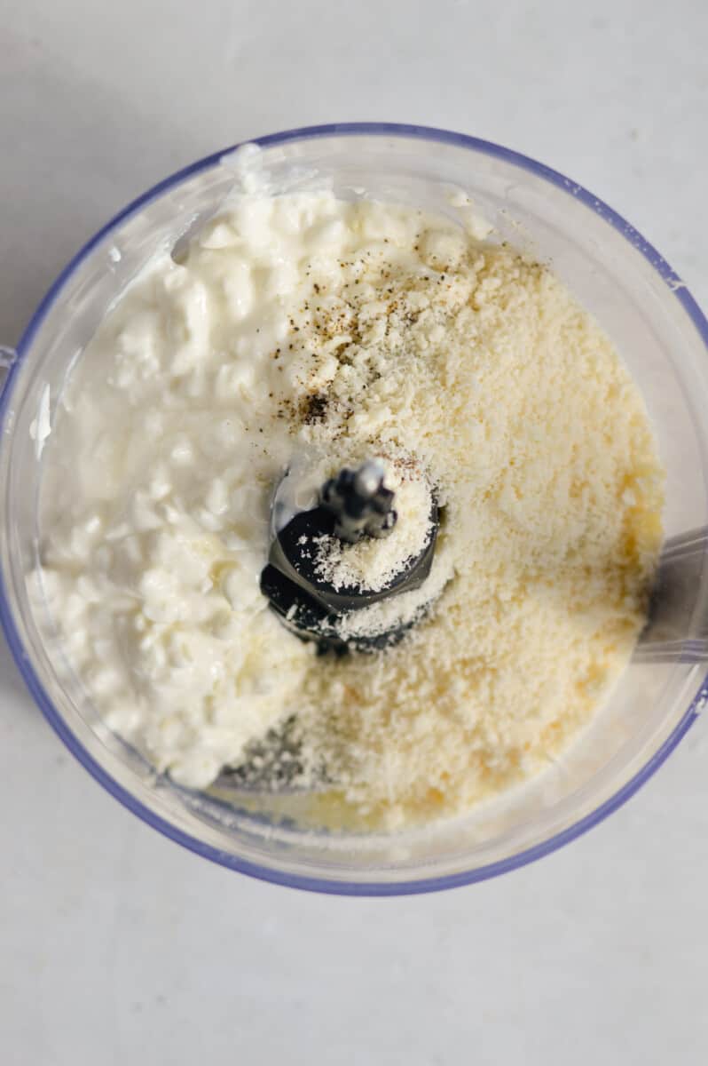 Adding olive oil, cottage cheese, parmesan cheese, garlic, salt and black pepper to a food processor.
