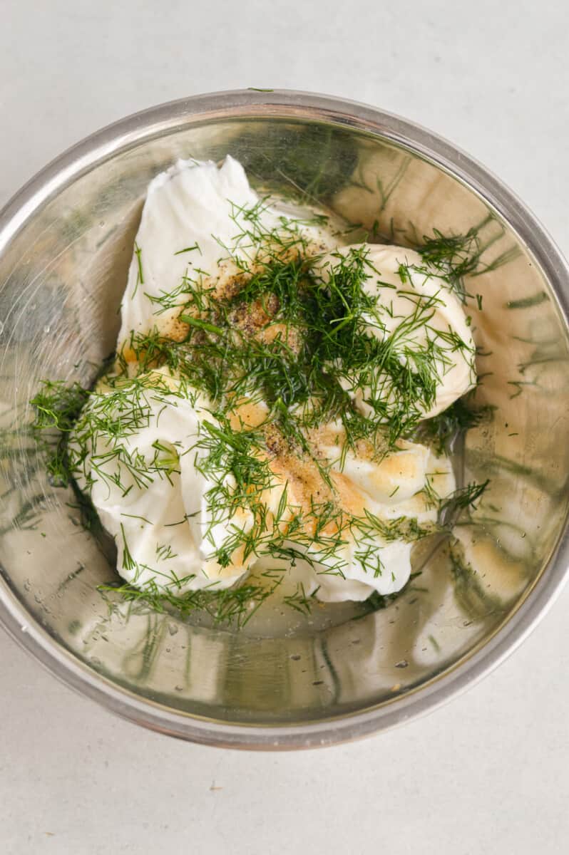 Adding (yogurt, mayonnaise, fresh dil, salt, pepper, garlic powder onion powder and lemon juice to a metal bowl.