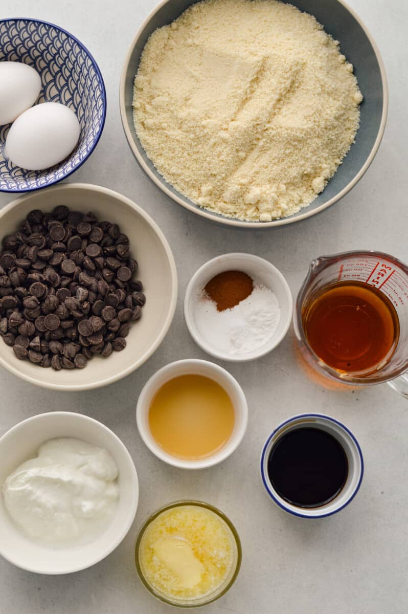Ingredients including almond flour, chocolate chips, baking powder, baking soda, maple syrup, apple cider vinegar, cinnamon, salt, butter, Greek yogurt.