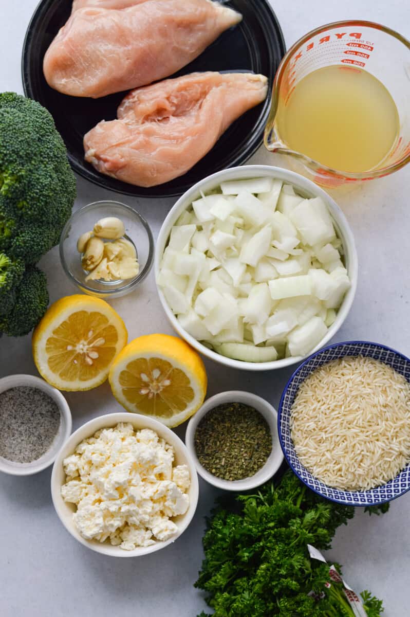 Ingredients including chicken, broccoli, broth, onion, rice, lemon, seasoning, feta, olive oil and garlic.
