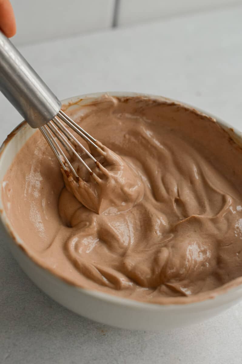 Whisking together Greek yogurt and chocolate protein powder to create chocolate Greek yogurt.