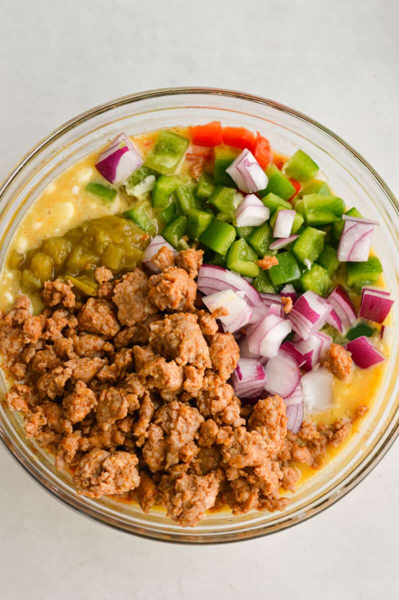 Adding cooled cooked sausage meat, diced peppers, onions and green chilies to egg mixture.