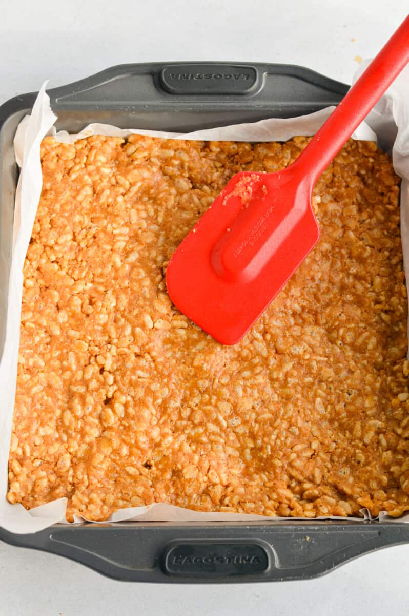 Pressing the rice krispie mixture into a parchment paper lined 8x8’ baking dish.