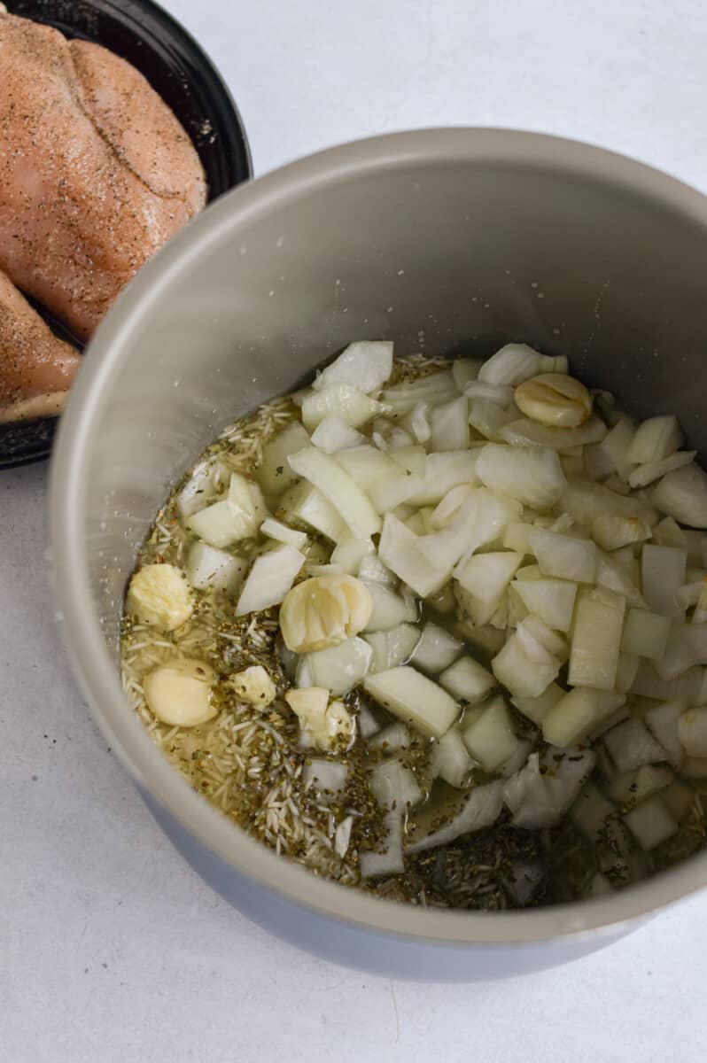 Adding rice, chicken broth, diced onion,  smashed garlic, oregano and basil to a crockpot.