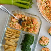 Adult lunchable with spicy tuna salad, cucumbers and crackers next to a bowl of tuna salad and bunch of green onions.