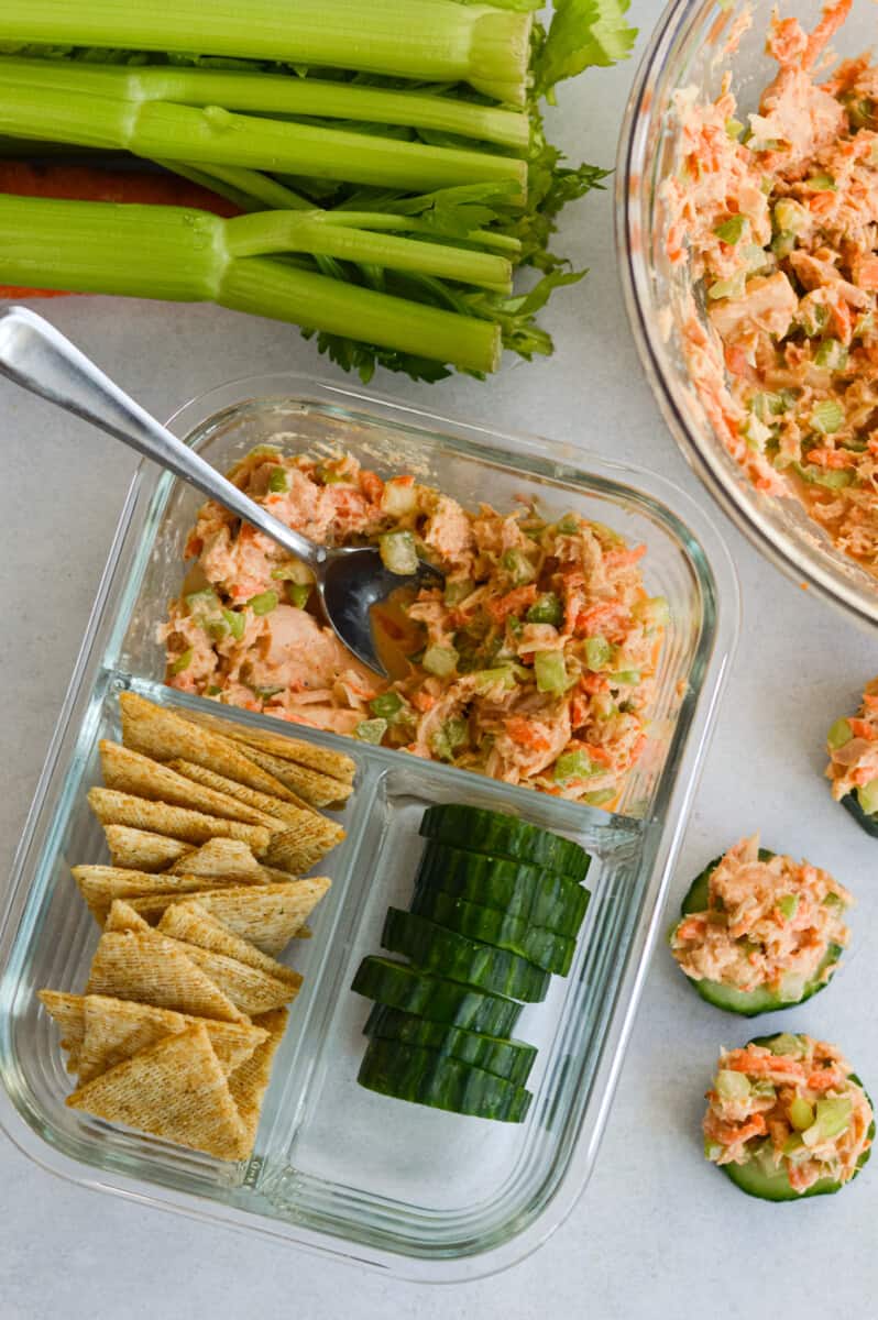 Adult lunchable with spicy tuna salad, cucumbers and crackers next to a bowl of tuna salad and bunch of green onions.