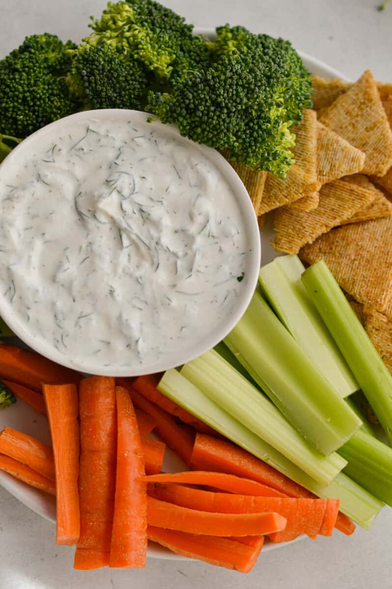 Plate with celery sticks, carrot sticks, broccoli, crackers and Greek yogurt dill dip.