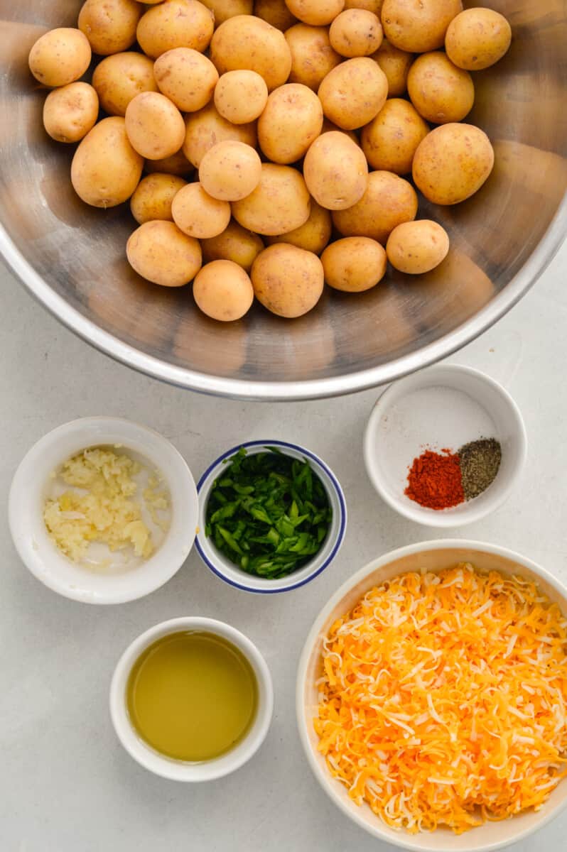Ingredients including baby potatoes, shredded cheese, olive oil, seasoning, garlic and chives.