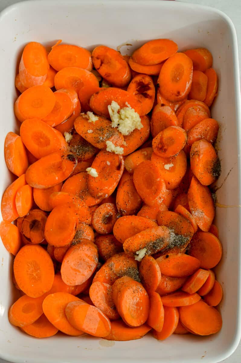 Adding olive oil, honey, balsamic vinegar, salt, pepper, red pepper flakes, and garlic to sliced carrots.
