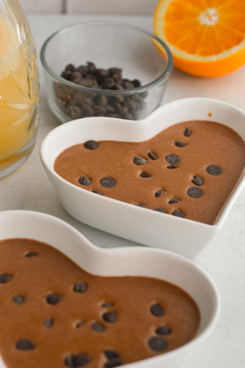 Adding chocolate chips to chocolate baked oat batter in ramekins.