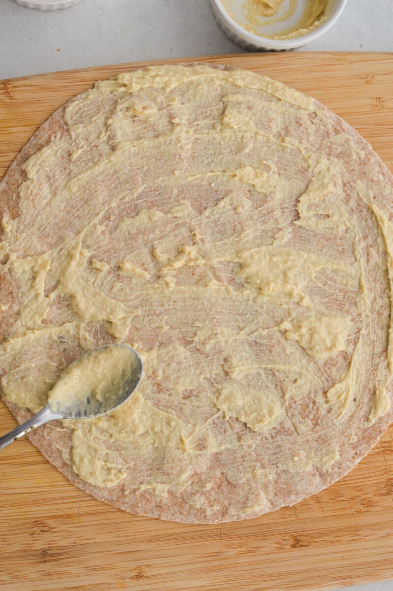 Spreading hummus on a whole wheat tortilla.