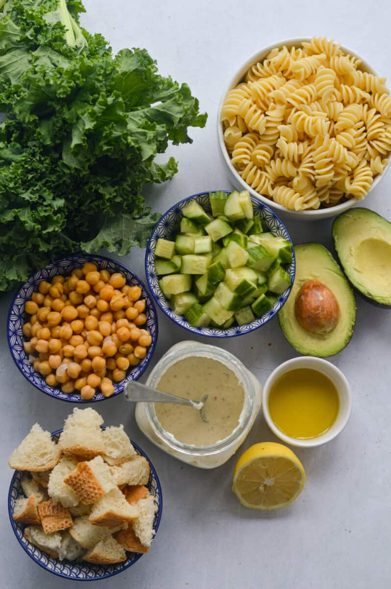 Ingredients including kale, avocado, chickpeas, pasta, sourdough croutons, Caesar dressing, lemon and olive oil.