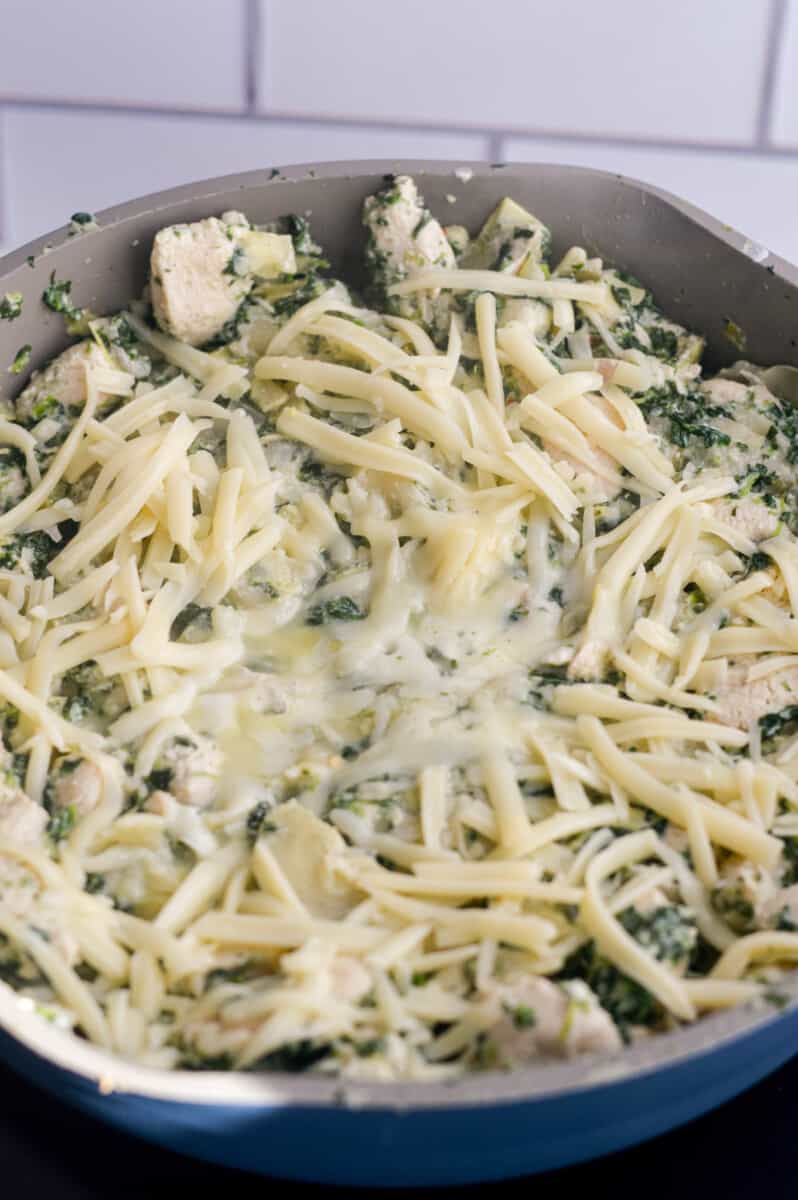 Topping spinach artichoke pasta with shredded mozzarella.