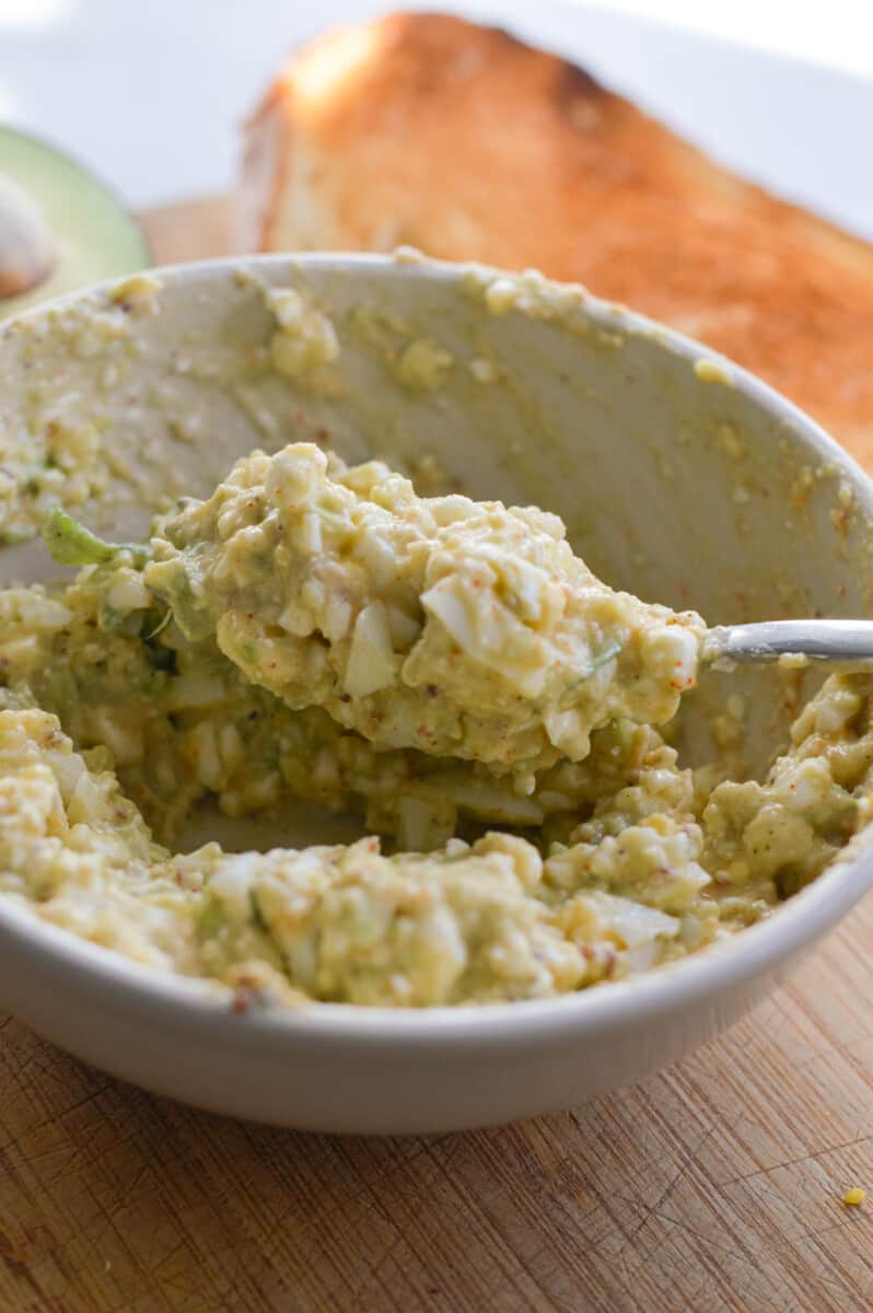 Mashing avocado, cottage cheese, egg, dijon mustard and spices in a bowl.
