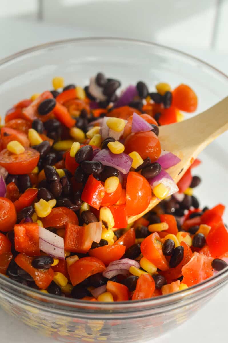 Mixing veggies, black beans and corn with olive oil and seasoning.