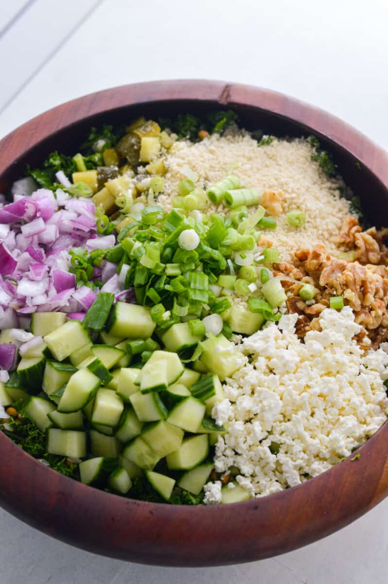 Adding cucumber, walnuts, panko breadcrumbs, lentils, feta cheese, dill pickles, green onions, fresh dill, and red onions to salad base.