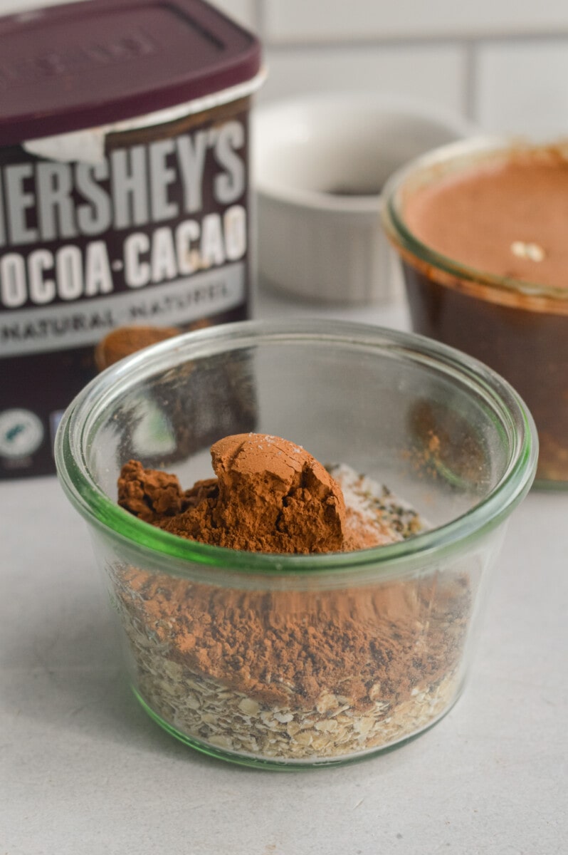 Adding oats, chia seeds, chocolate protein powder, cocoa powder and salt to a jar.