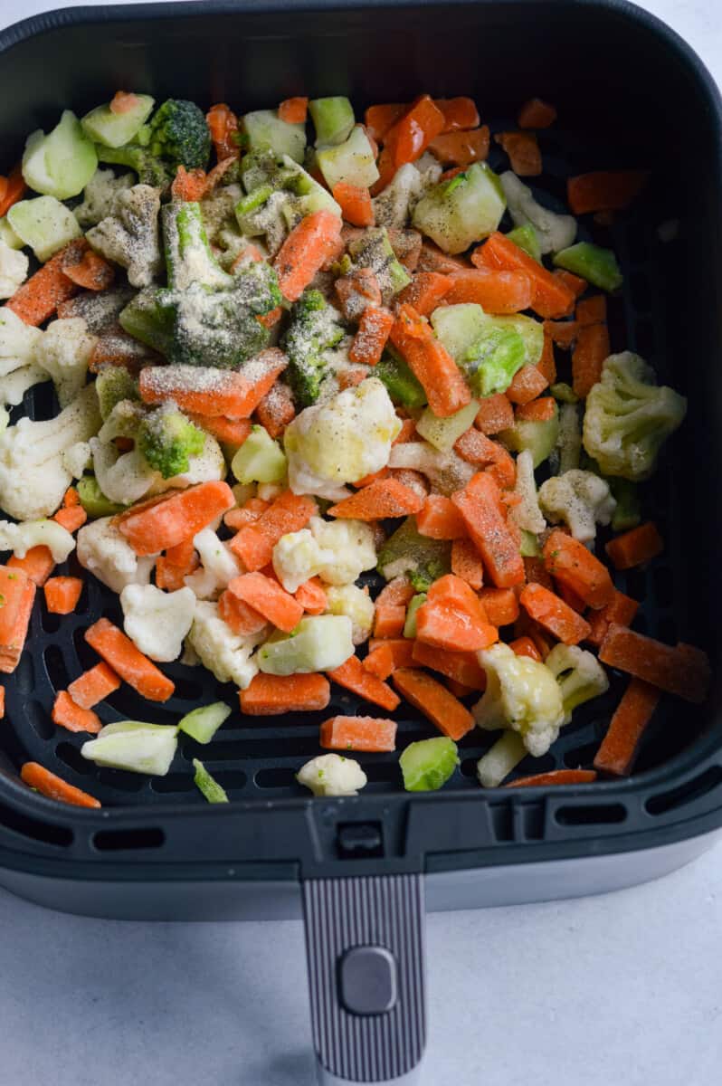 Adding frozen vegetables to air fryer basket.