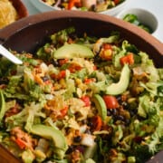 Bowl of nacho salad with ground turkey, avocado, tomatoes, cheese and tortilla chips.