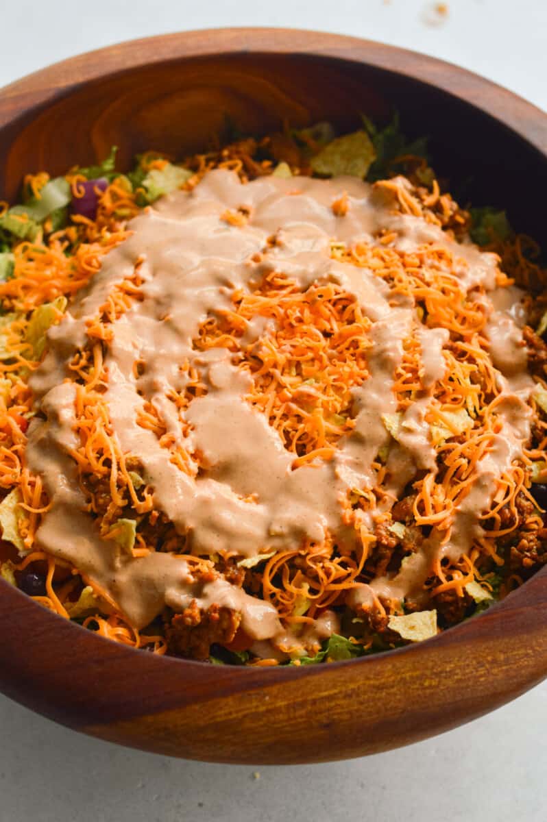 Adding salsa dressing to a cheesy nacho salad.