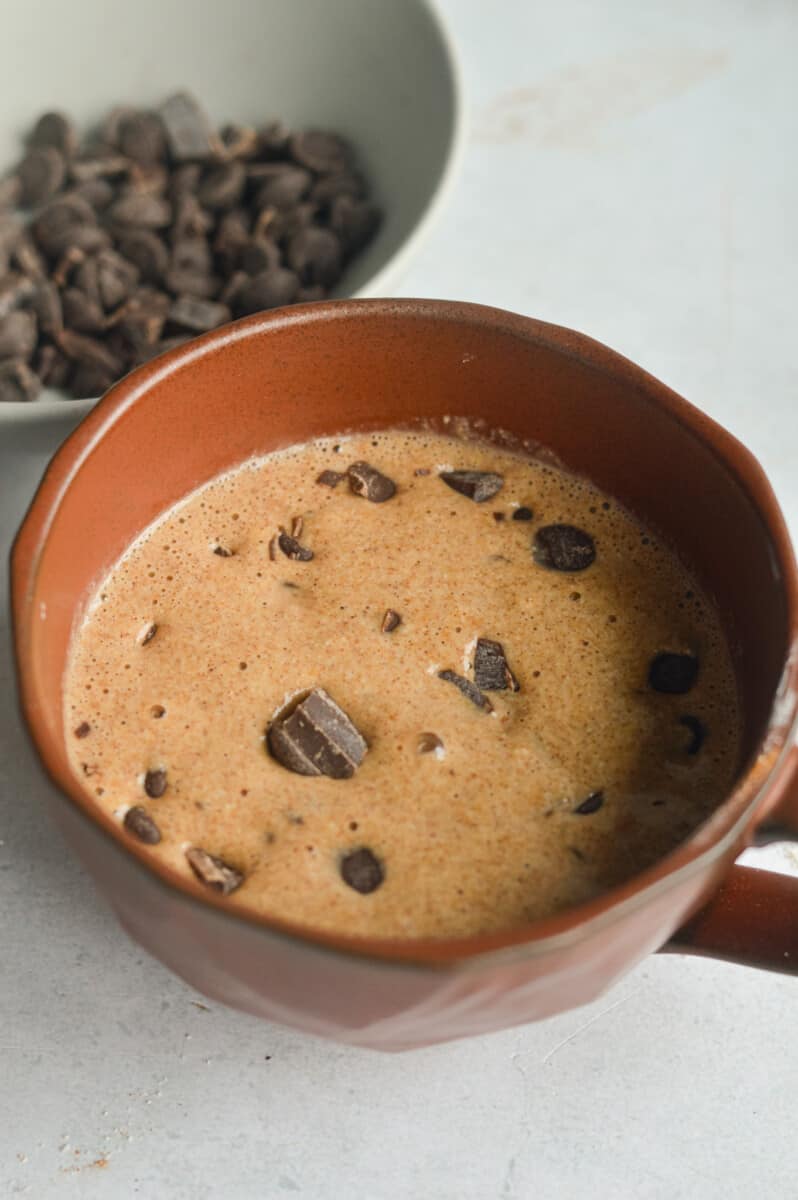Mixing chocolate chunks into oatmeal mug cake batter.