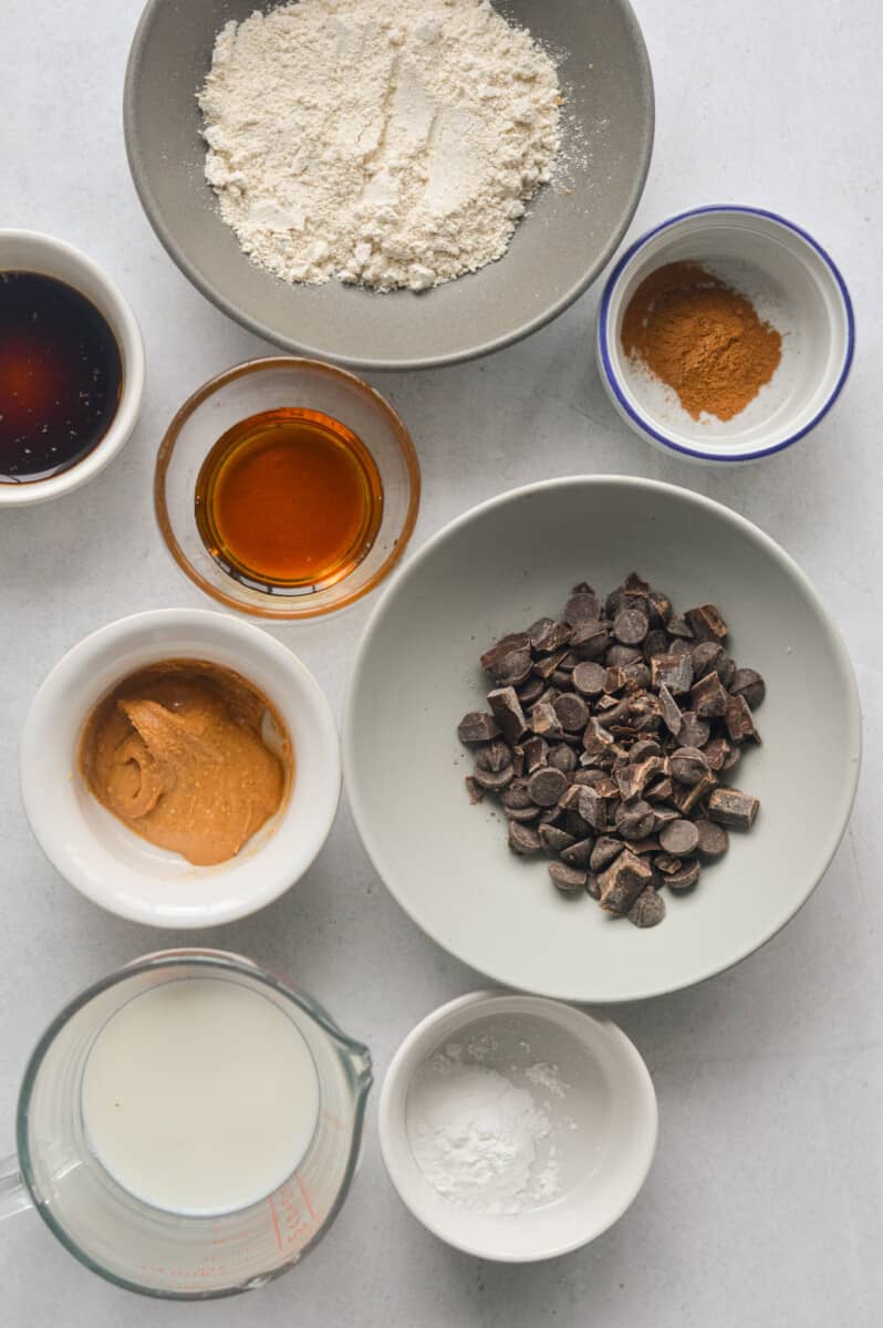 Ingredients including chocolate chips, oat flour, maple syrup, nut butter, baking powder, milk and cinnamon.