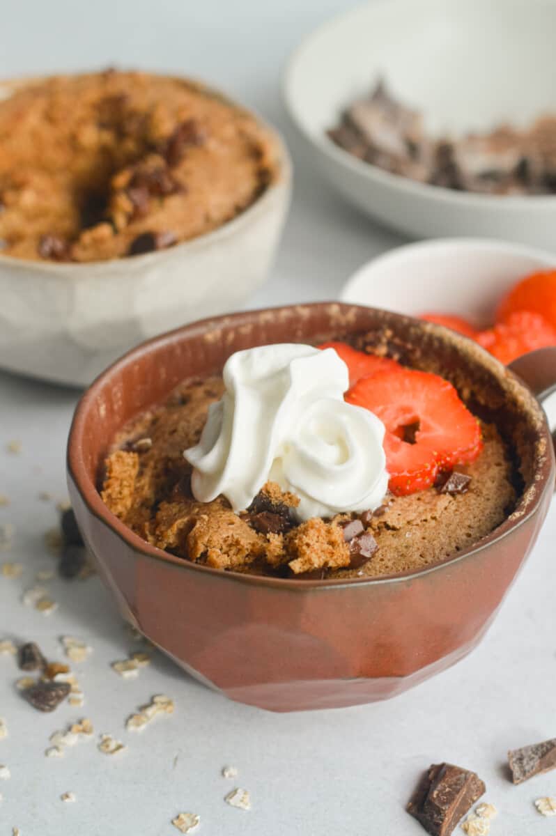 Oatmeal mug cake topped with whipped cream and berries.