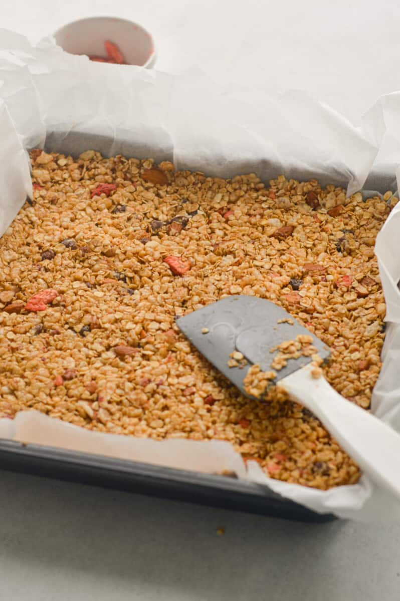 Pressing granola bar mixture into a square pan lined with parchment paper.