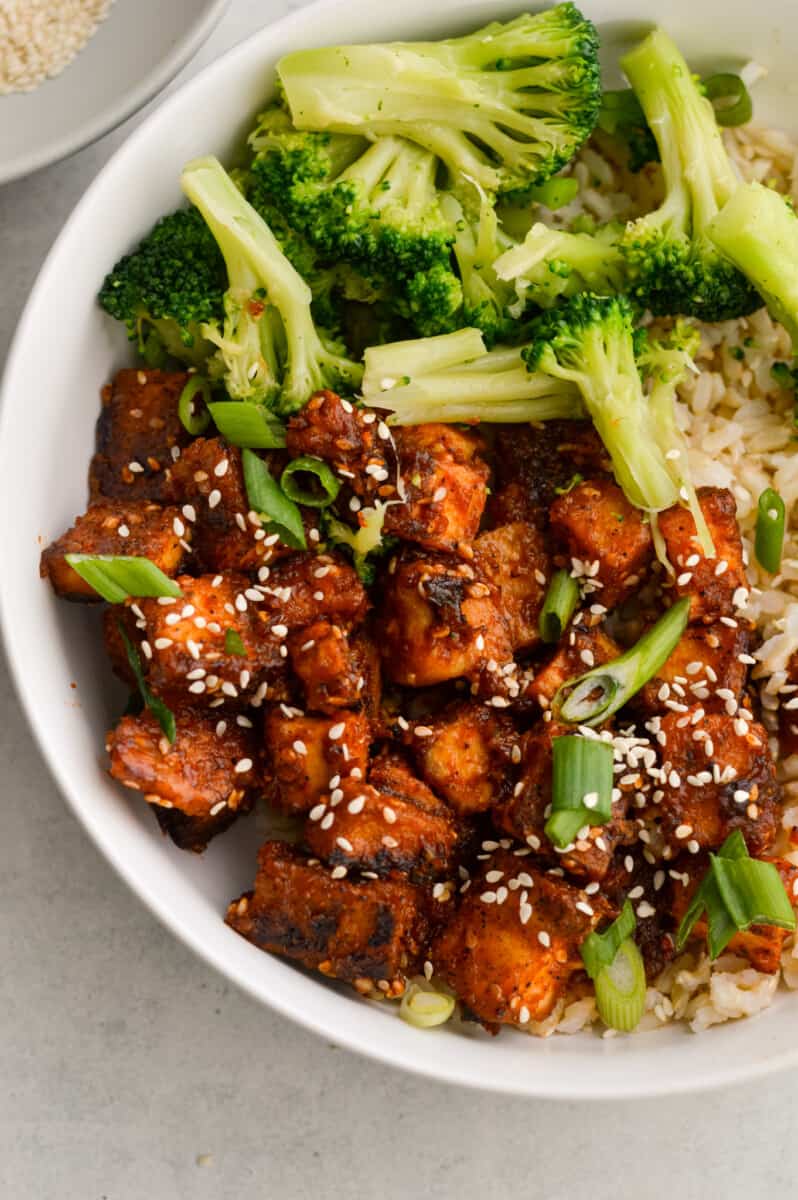Close up of sticky orange tofu in a bowl with brown rice and broccoli.