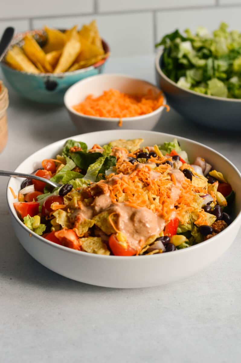 White bowl with nacho salad with cheese, tortilla chips, turkey and creamy salsa dressing.
