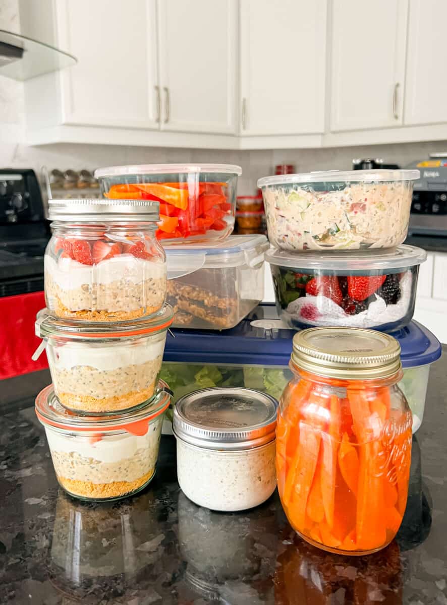 Containers of meal prep overnight oats, carrot sticks, berries and other meals and snacks.