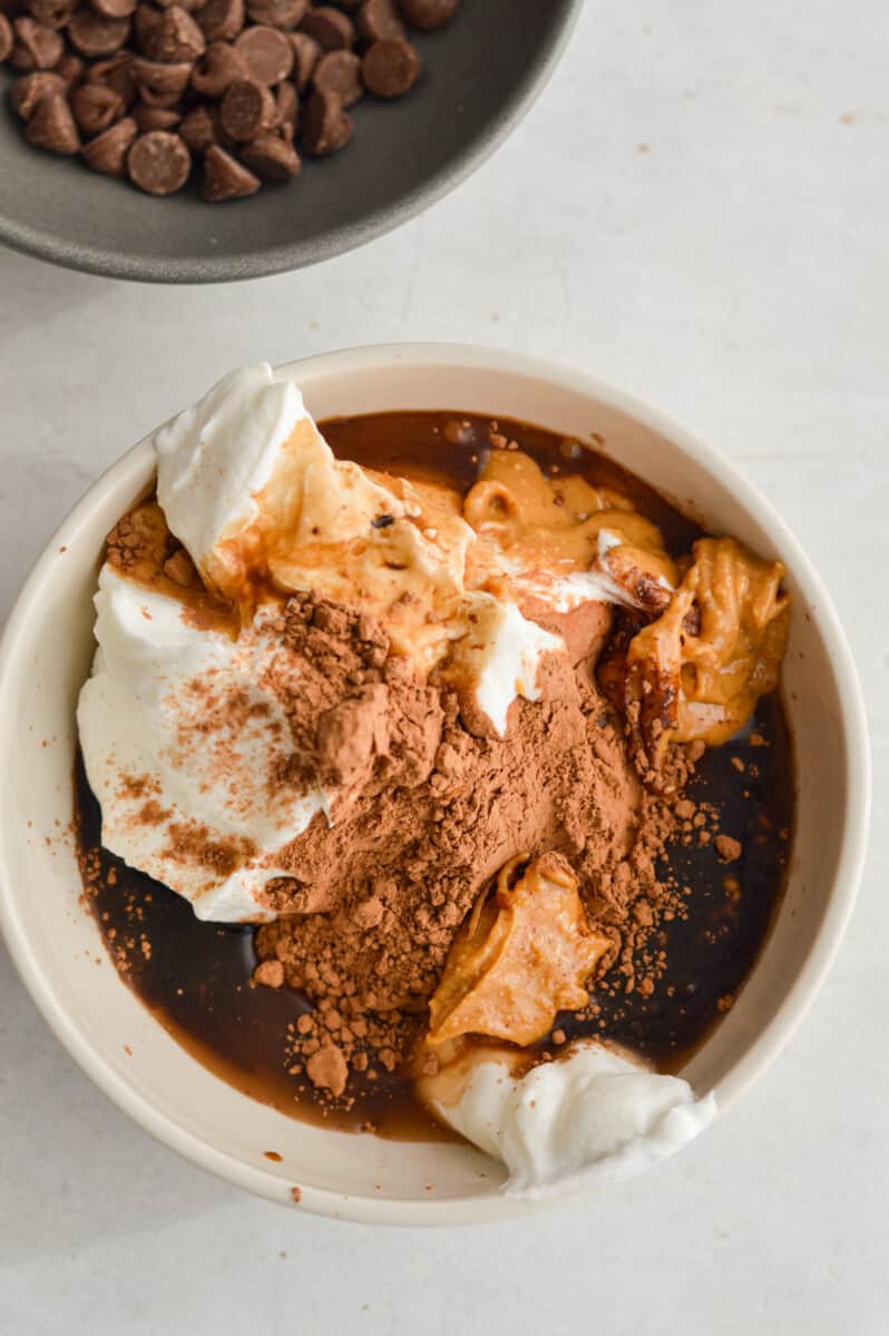 Adding greek yogurt, cocoa powder, maple syrup, vanilla extract and peanut butter to a bowl.