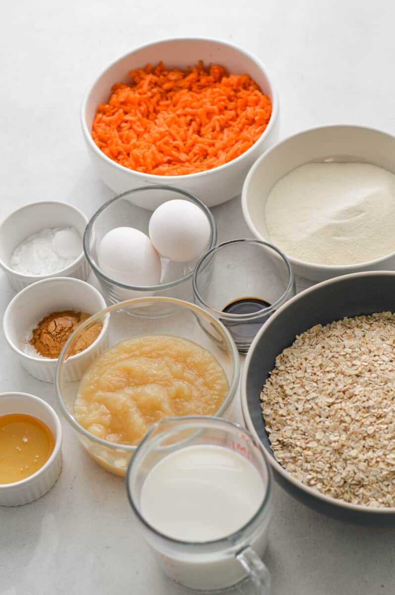 Ingredients measured out including oats, collagen, shredded carrots, eggs, spices, applesauce, honey and milk.