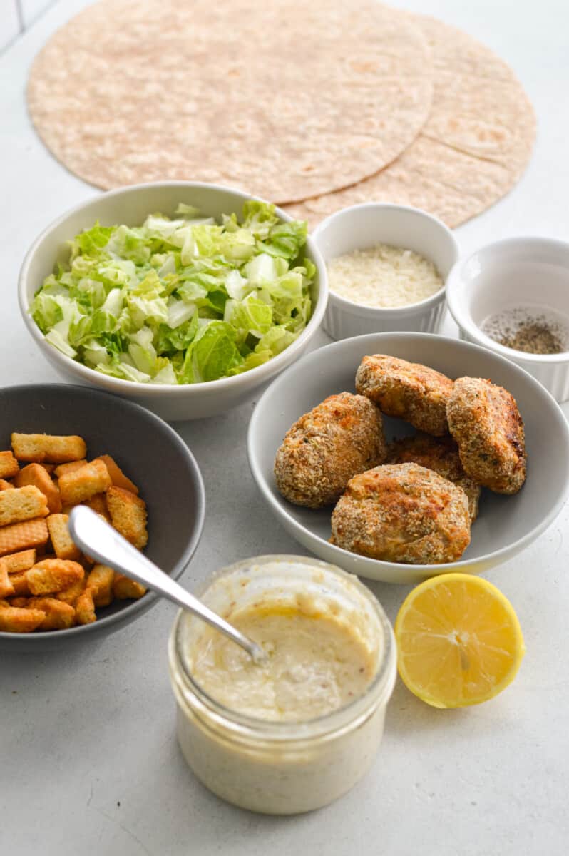 Ingredients including romaine lettuce, homemade chicken nuggets, Greek yogurt Caesar dressing, lemon, croutons and whole wheat tortillas.