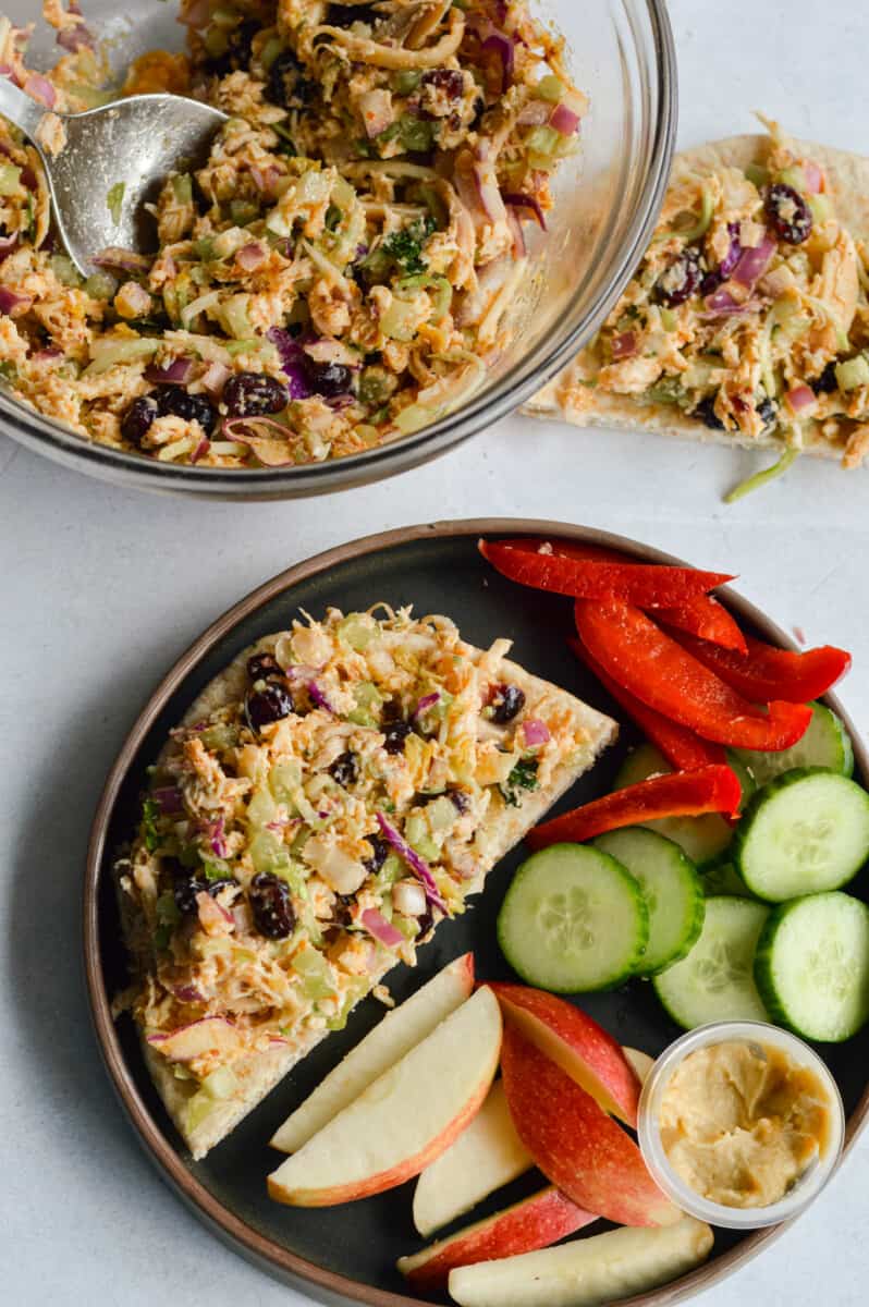Birds eye of a lunch plate with chicken salad on toast, chopped veggies and a sliced apple.