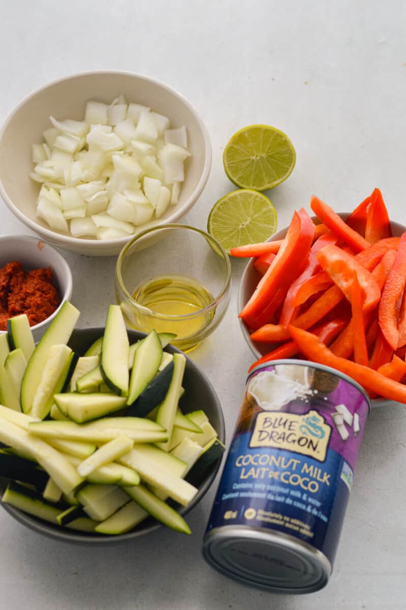 Ingredients including coconut milk, bell pepper, zucchini, onion, lime, olive oil and red curry paste.