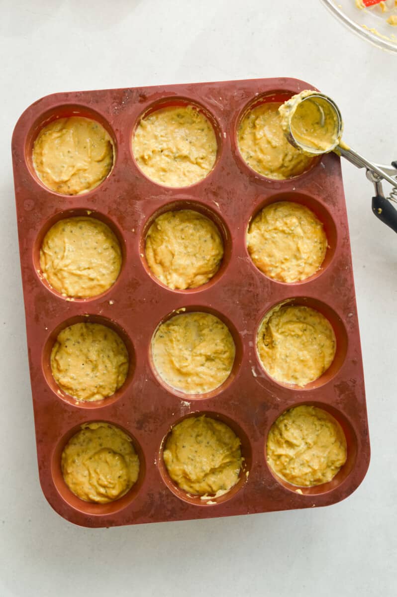Filling a muffin tin with lemon muffin batter.