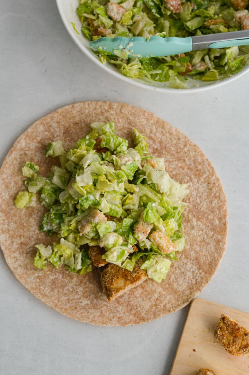 Assembling Caesar chicken nugget wrap in a whole wheat tortilla.