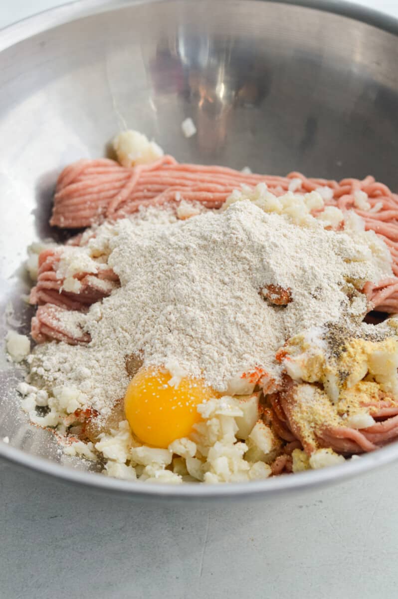 Mixing ground chicken egg, spices, riced cauliflower and oat flour.  