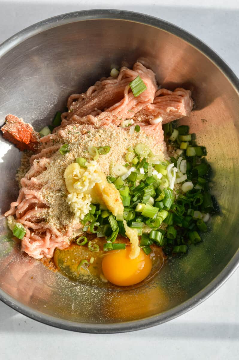 Mixing ground chicken, garlic, ginger, green onions, egg, breadcrumbs, soy sauce and red curry paste.