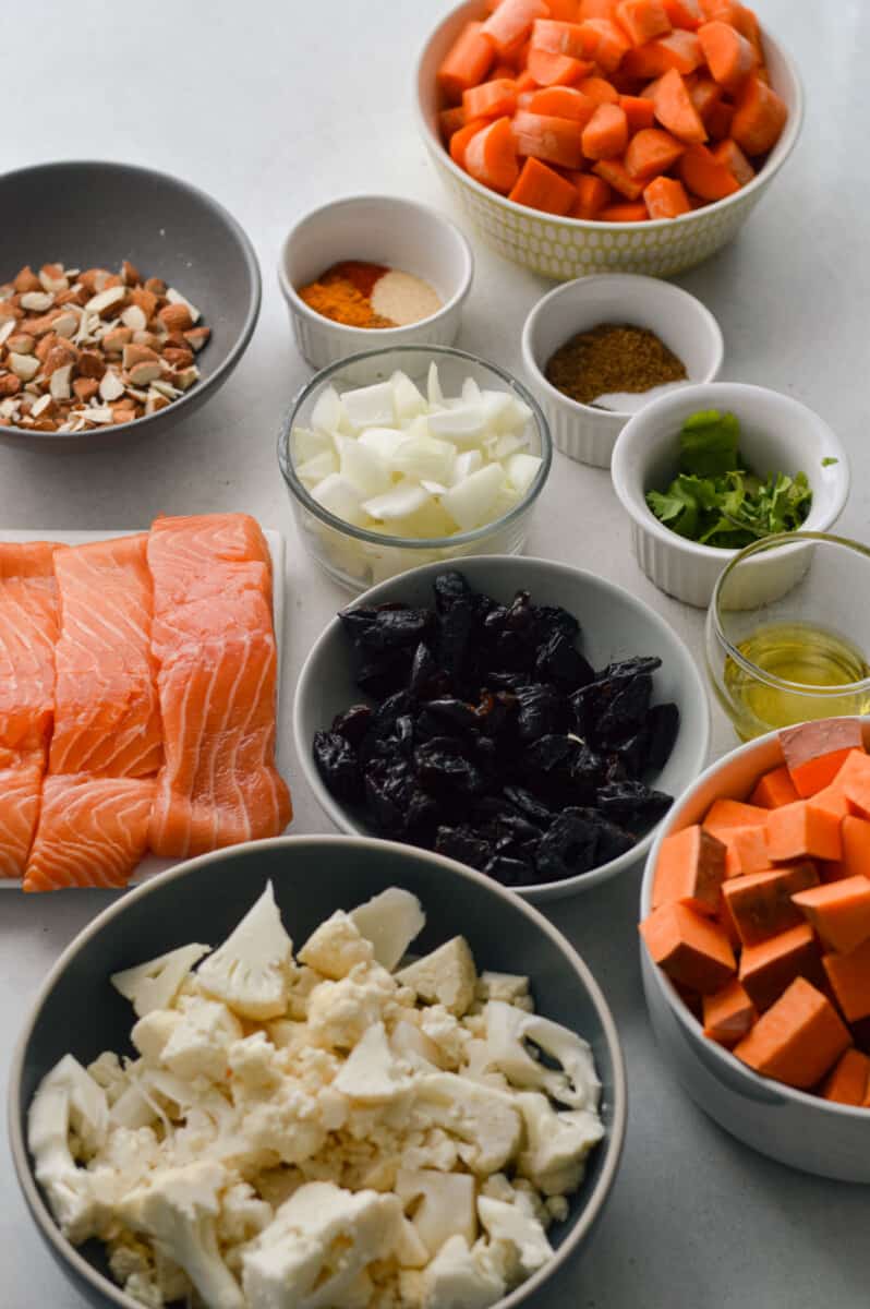 Ingredients including salmon, sweet potato, carrot, cauliflower, almonds, prunes, onion, olive oil and spices.