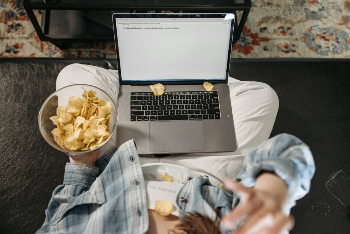 Birds eye of a girl snacking mindlessly on popcorn while scrolling on her laptop.