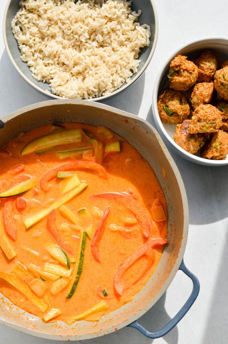 Bowl of rice, pot of Thai red curry and bowl of ginger chicken meatballs.