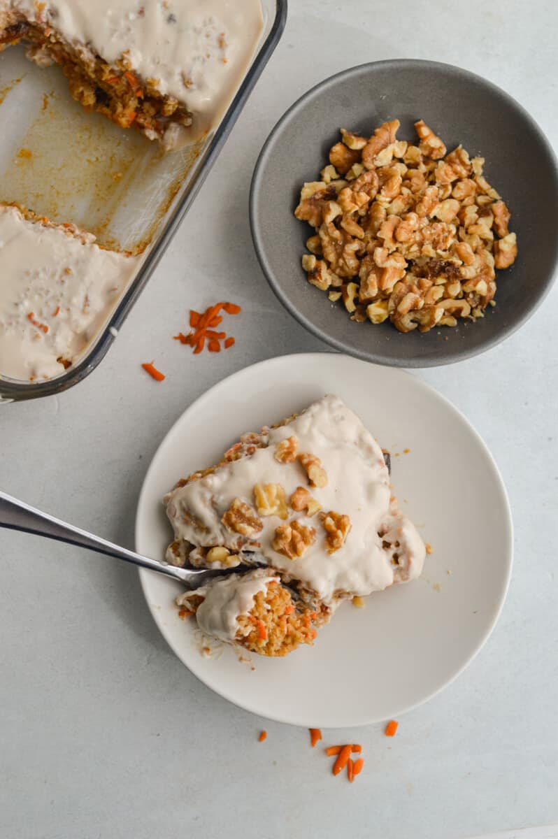 Plate with a slice of carrot cake baked oatmeal next to a bowl of walnuts.