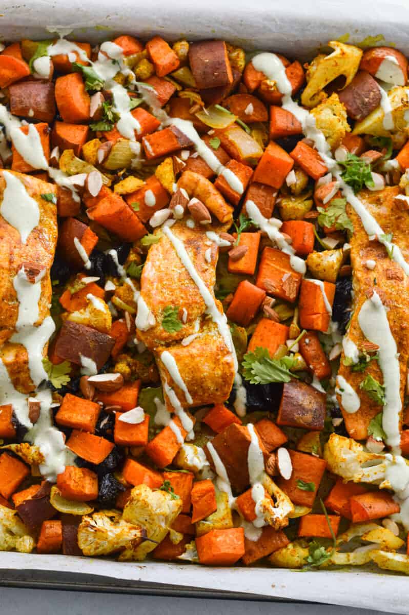 Drizzling yogurt sauce on sheet pan moroccan salmon and vegetables.