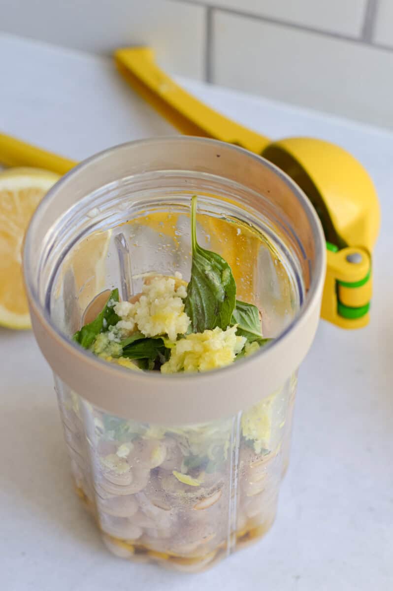 Adding lemon juice and zest, white beans, nasil, olive oil and salt and pepper into a blender.