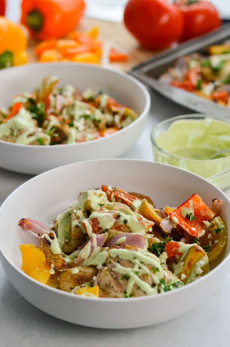 Bowls of herb and lemon chicken and bell peppers, drizzled with green whipped feta sauce.
