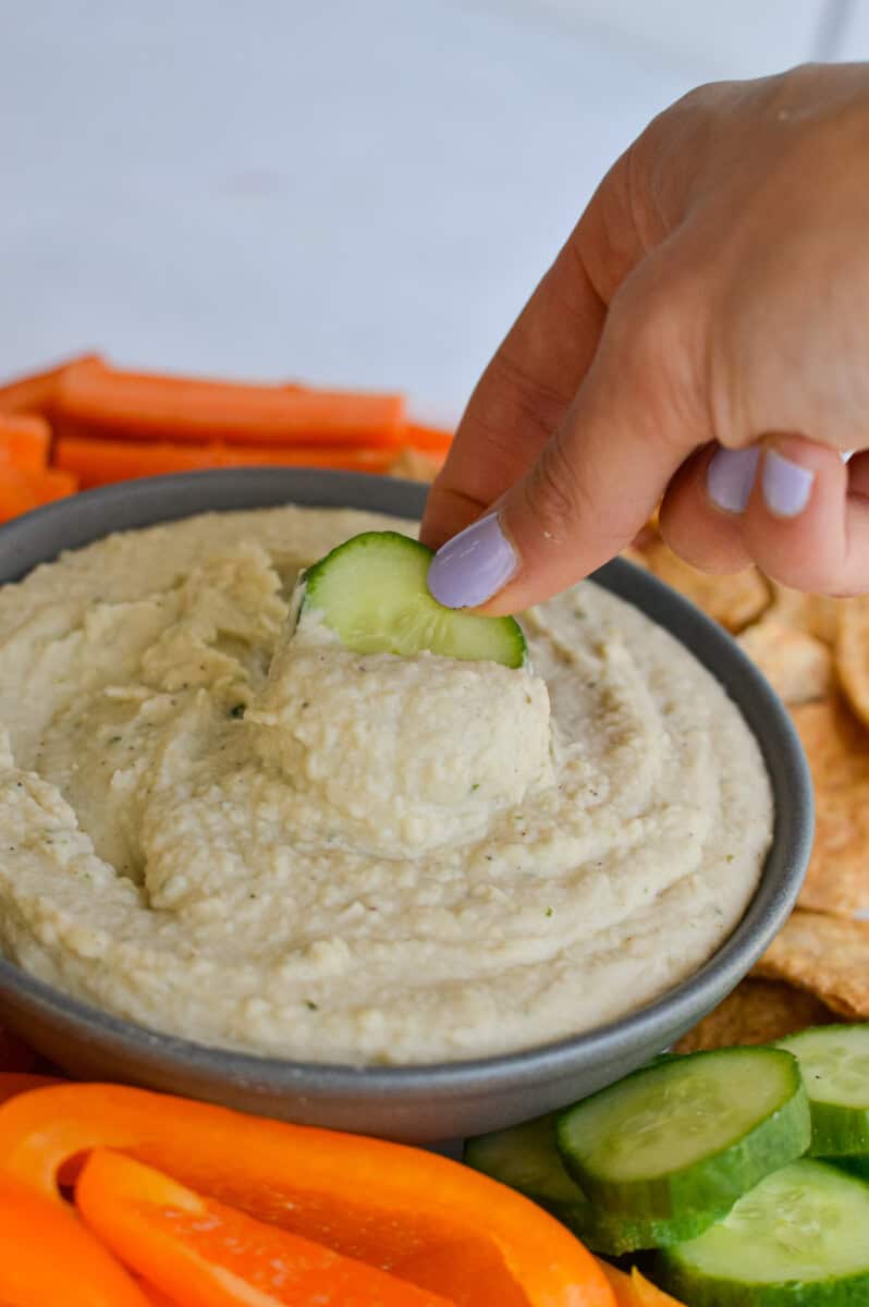 Dunking a cucumber into white bean dip.