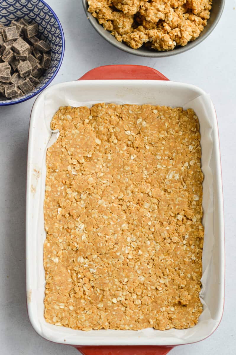 Pressing first layer of oat mixture into a baking tray.