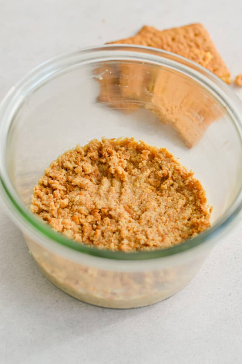 Pressing a graham cracker crust into the bottom of a glass jar.
